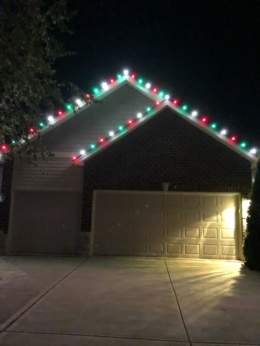 House decorated with red and green Christmas lights along the roofline at night.